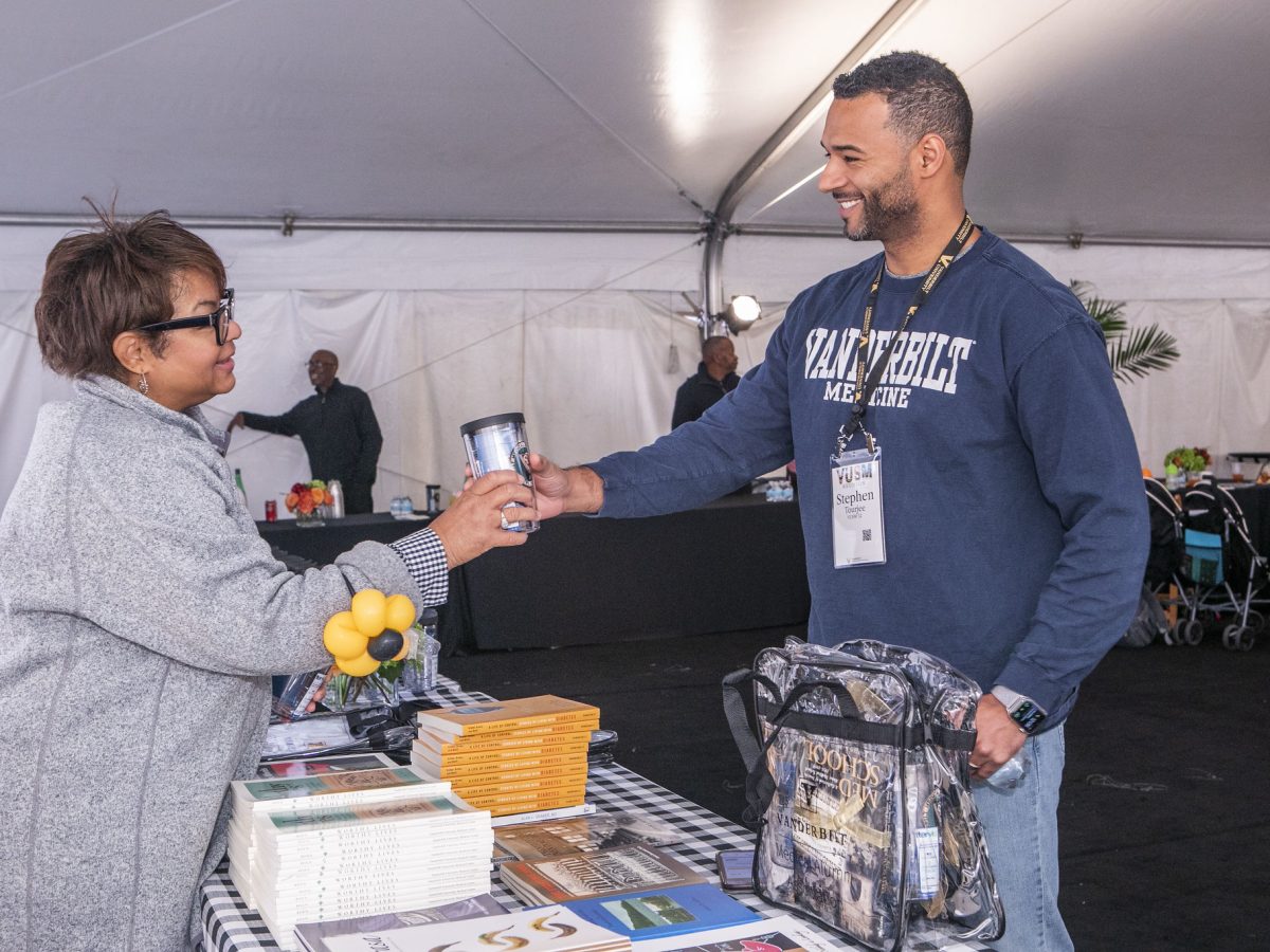 VUSM Student Affairs staffer Portlyn Cruise volunteers at Reunion. A woman hands a man a souvenir tumbler at an event.