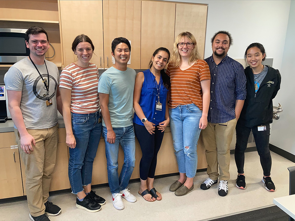 Group photo of Byndloss lab members standing in a break room. Two of the women are wearing horizontal striped shirts.