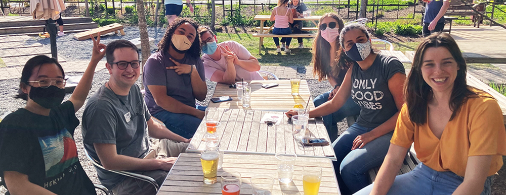 Photograph of Byndloss lab members sitting around an outdoor dining table. All but two of them are wearing face masks.