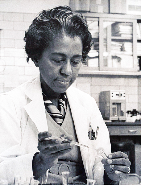 Photo of Marie Maynard Daly at a lab bench extracting liquid from a test tube.