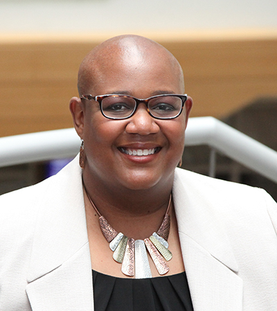 Headshot of Felysha Jenkins. She is wearing eyeglasses, a metal necklace, a black top and a white coat. A white hand rail is in the background.