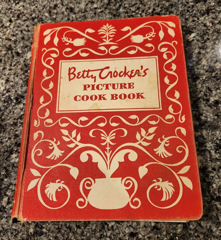 An old, bound book titled "Betty Crocker's Picture Cook Book," which has a red cover.