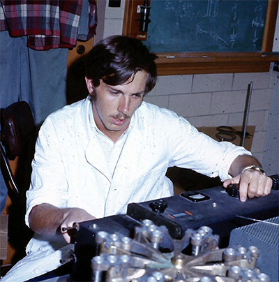 A young Guengerich concentrates on the machine he is operating, which is sitting on a lab bench in front of him.