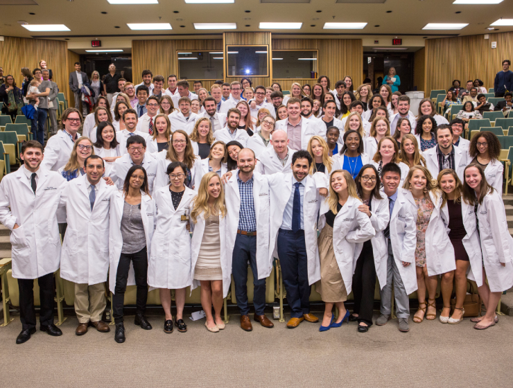 A large group of lab coat-wearing graduate students in a lecture hall.