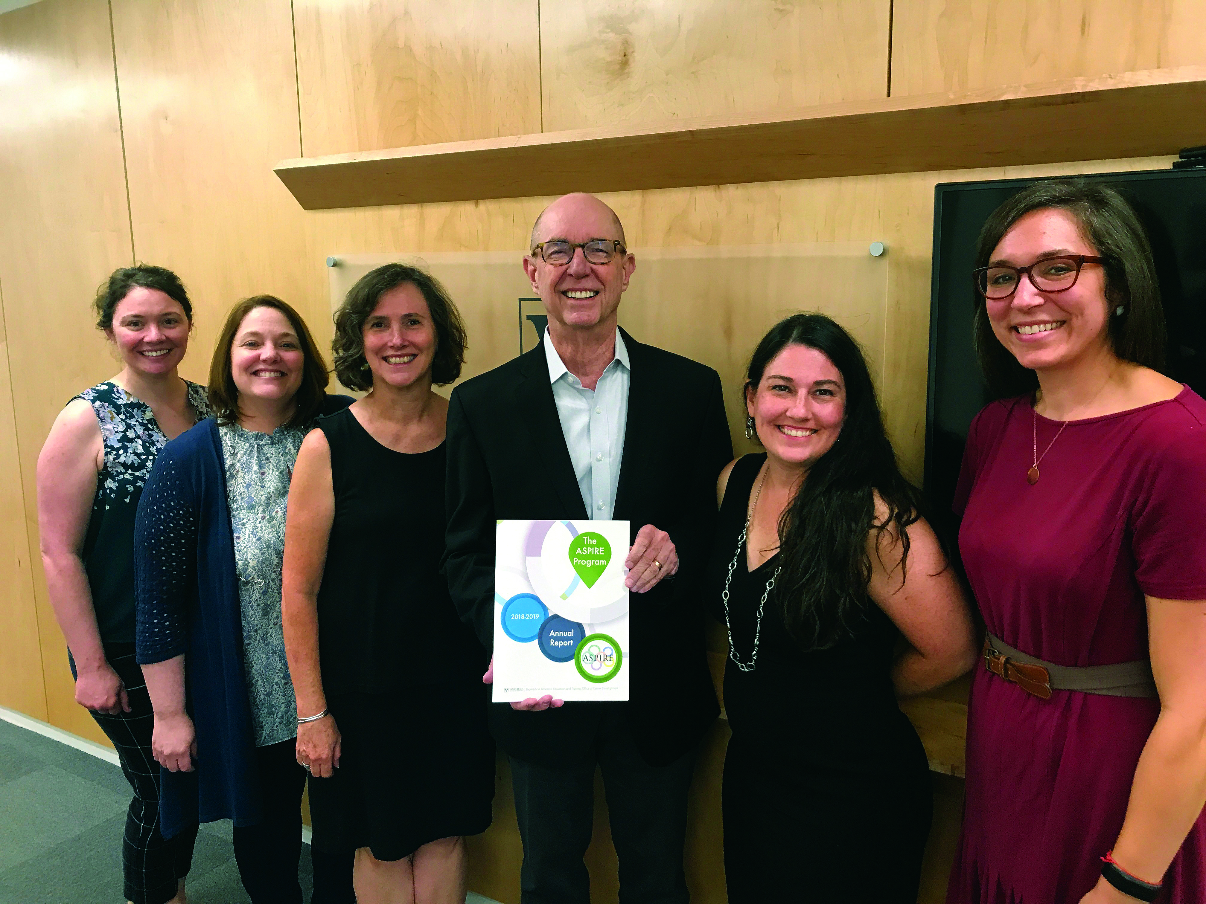 The staff of the BRET Office poses with Dean Larry Marnett, who is holding the 2018-2019 ASPIRE Annual Report. From left, Angela Zito, Kim Petrie, Kathleen Gould, Larry Marnett, Ashley Brady, and Kate Stuart.