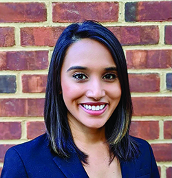 Headshot of Turnee Malik. She is wearing a navy blue jacket and is standing in front of a brick wall.