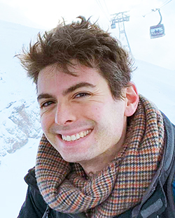 Close-up of Diego del Alamo, who appears to be on a ski lift. He is wearing a gray jacket and a brown/black patterned scarf.