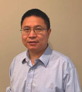 Guoqiang Gu wearing glasses and a light blue collared shirt with no tie and the top button open.