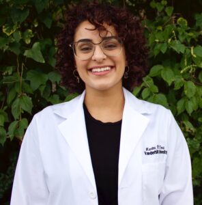 Marina Hanna standing in front of a hedge wearing glasses and a lab coat embroidered with her name.