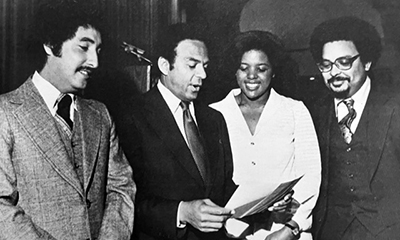 Black and white photo of Andrew Young (second from left to right), American politician, diplomat, and activist, congratulates Fant (far right) and other medical students for winning National Merit Foundation merit awards for academic excellence, leadership, and service. 