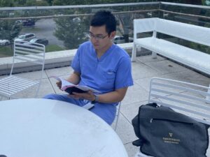 A student in scrubs reads an academic journal while sitting outside