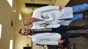 Two men standing in white coats, one short and one long.