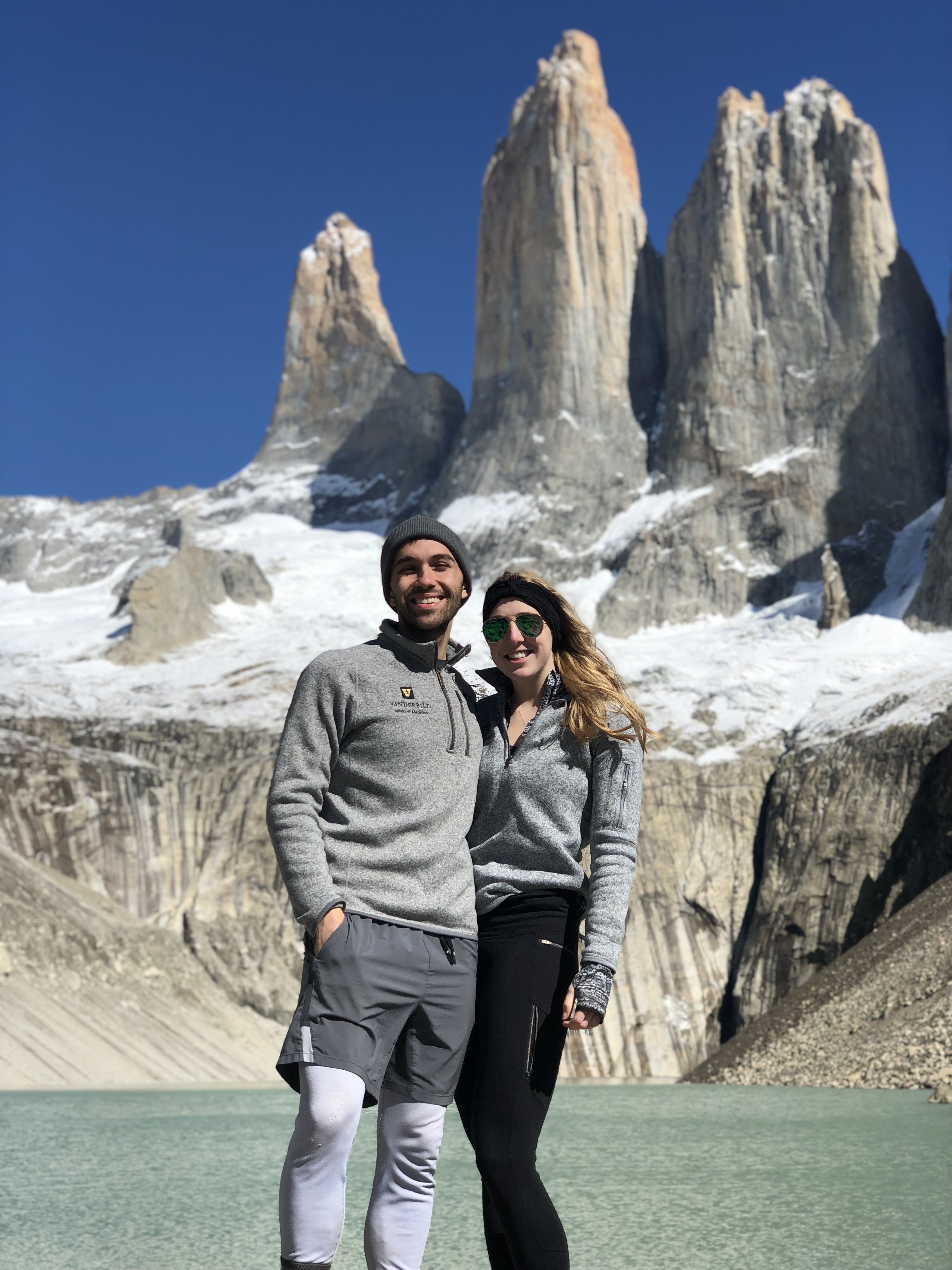 Two people in gray fleeces stand in front of a snowy mountain