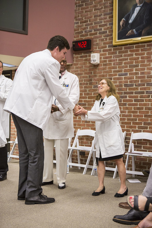 A man in a white coat bends down to shake hands with a woman in a white coat