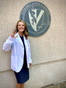 A woman in a white coat poses in front of a medical school outside seal