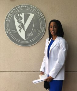 a woman in a white coat stands outside next to a medical school seal