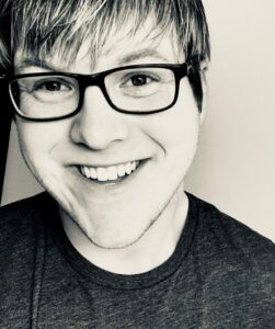 A man with glasses smiles. Black and white.
