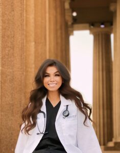 A woman in a white coat sits outside Parthenon columns