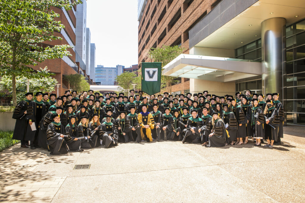MD Class of 2022 stands outside in their doctoral regalia with Dean Balser. VUMC buildings surround them.