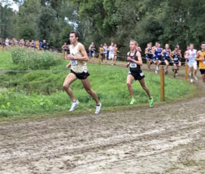 Men in NCAA uniforms race cross country on a dirt course