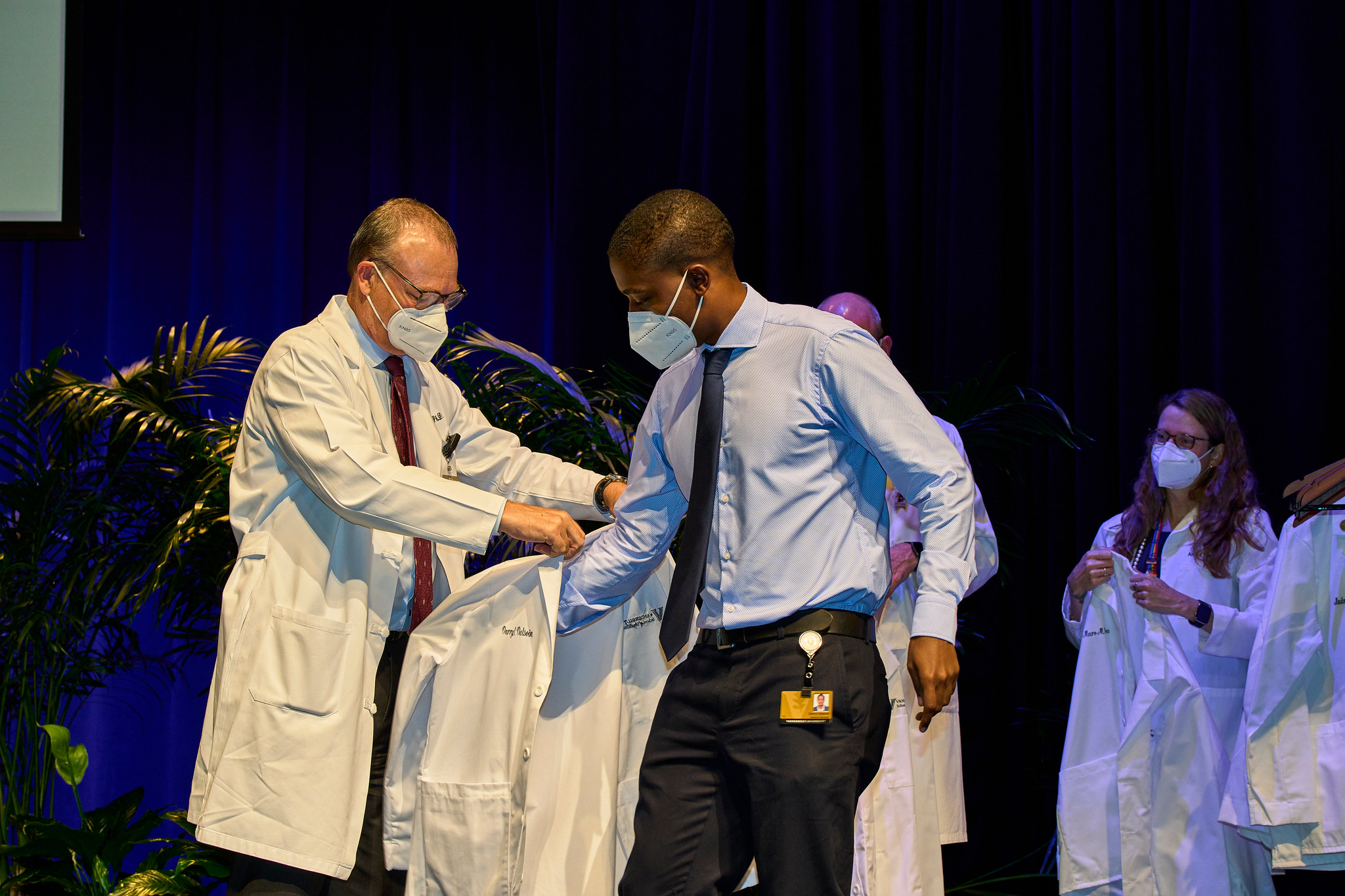 A man in a long white coat helps a student to put on a short white coat