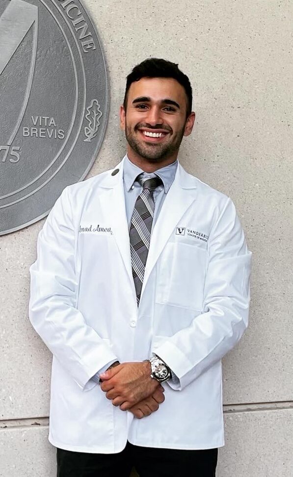 A man in a white coat and tie stands next to a medical school seal