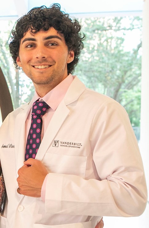 A man in a white coat and tie smiles