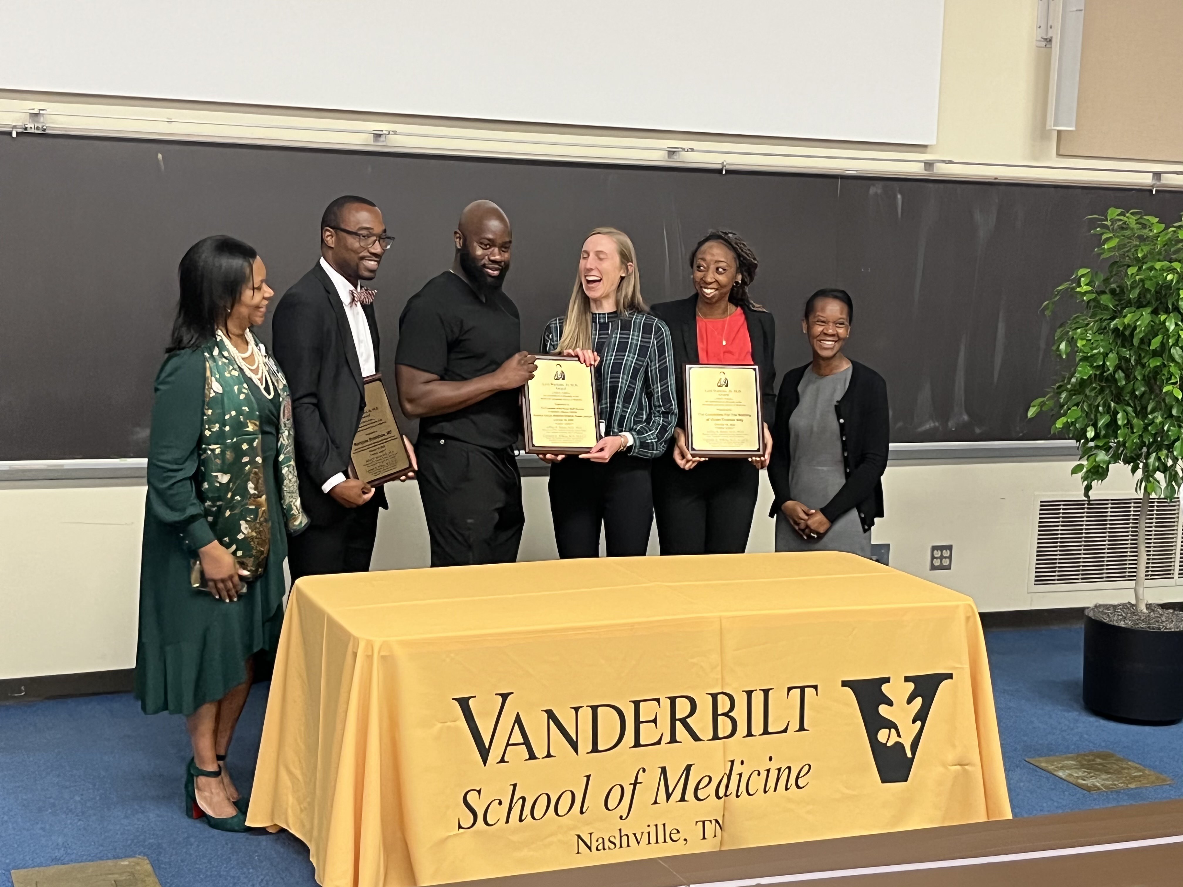 A group of students and faculty stand behind a table with a gold tablecloth that says "Vanderbilt School of Medicine"