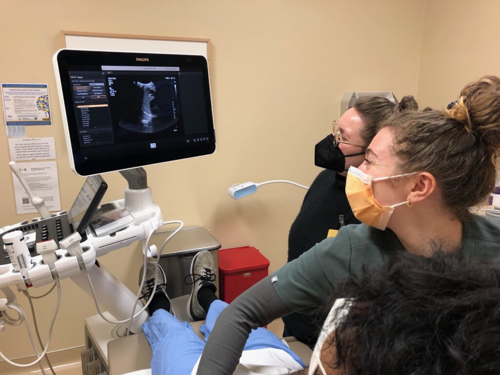 Two clinicians check an abdominal ultrasound while a person is on a table