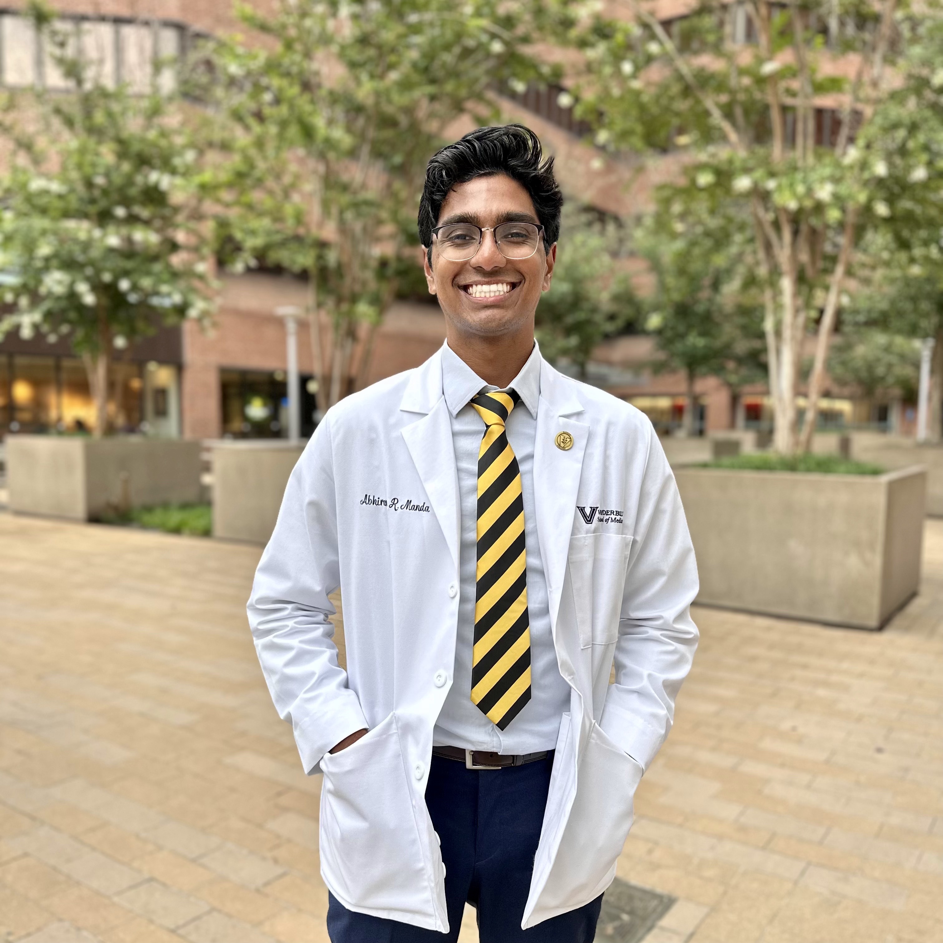 A medical student in a white coat smiles.
