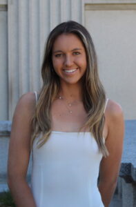 A woman in white stands outside and smiles