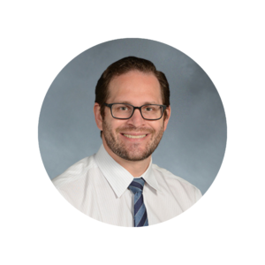 A man in glasses and a blue tie smiles