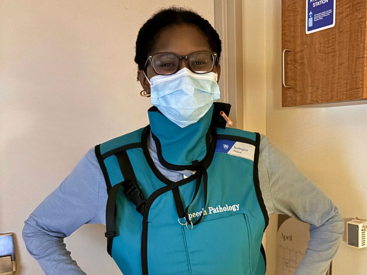 A smiling VUSM Speech-Language Pathology student wears a surgical mask and a protective lead vest