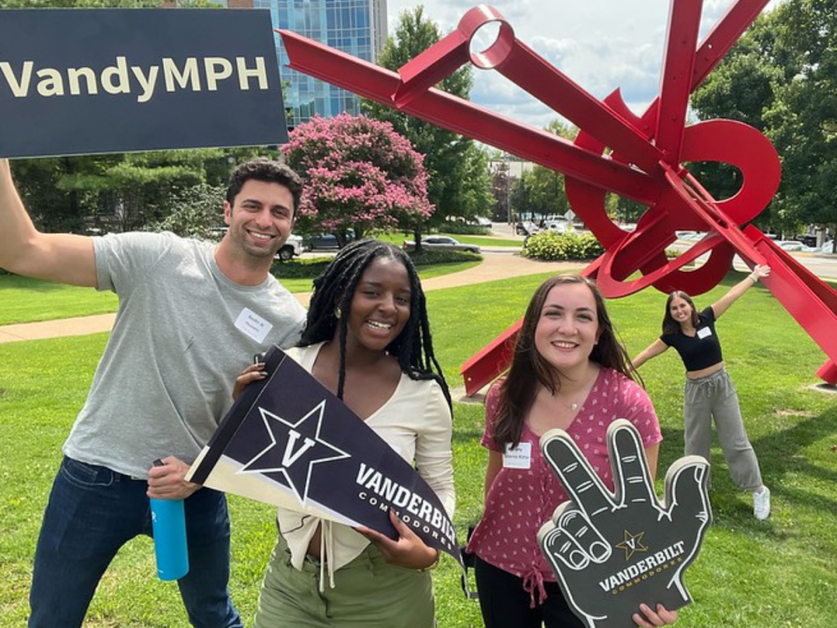 A group of VUSM students smiling while holding Vanderbilt University flags and signs outdoors on campus.