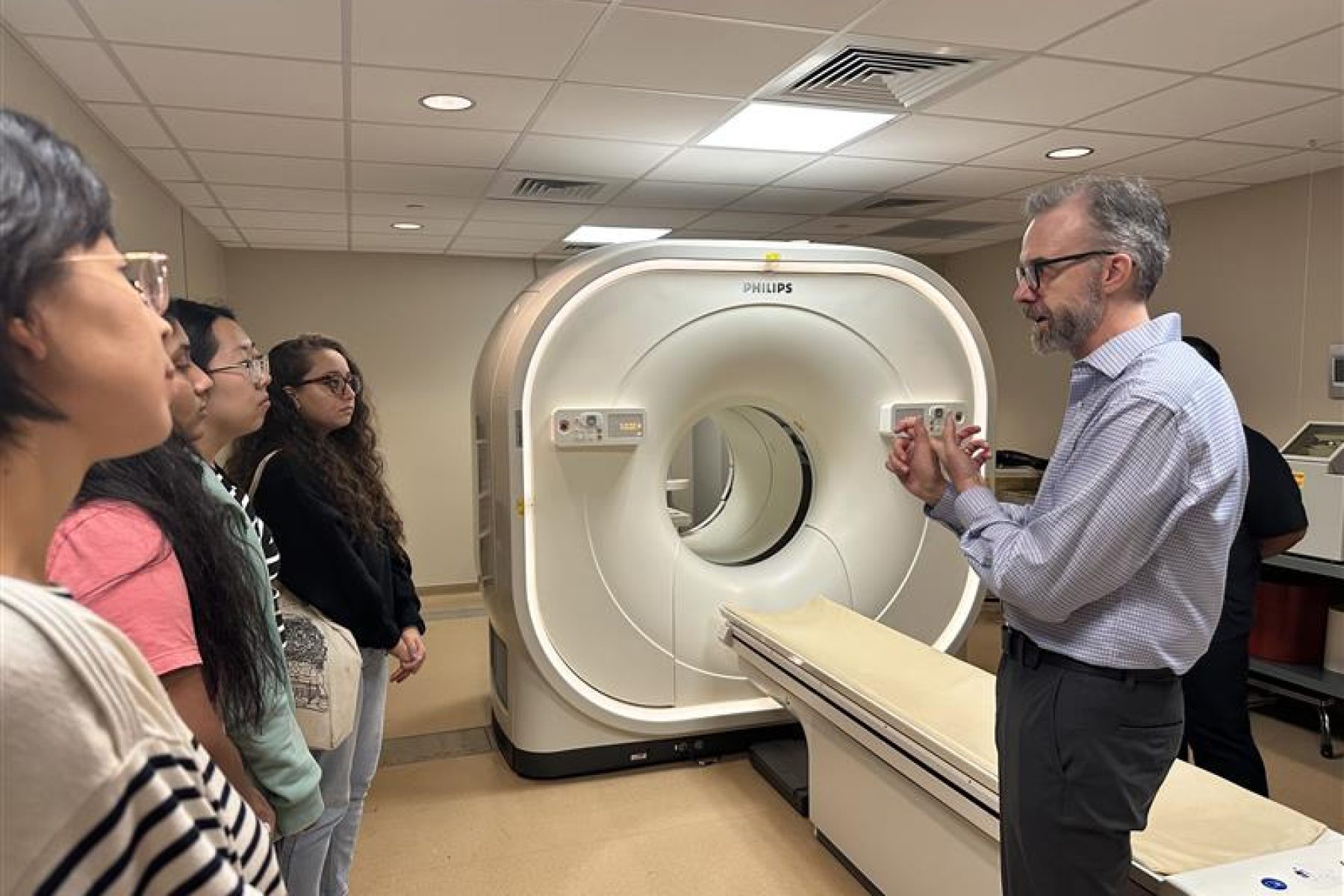 Students gather near a CT scanner for instruction from their professor.